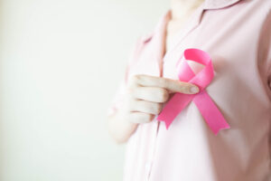 Close-up of a woman in a pink shirt holding a satin pink ribbon, symbolizing breast cancer awareness and support for those considering breast reconstruction after treatment.