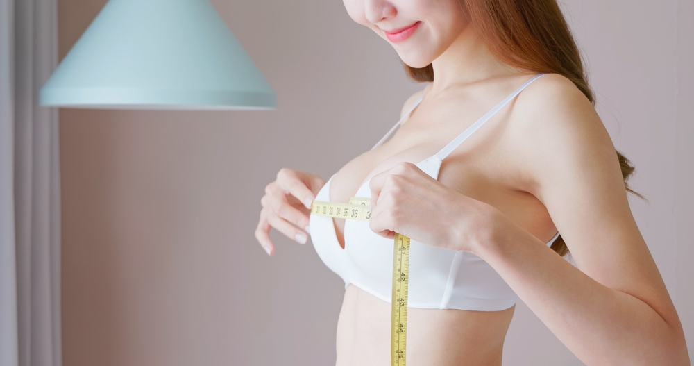 1770823829_shutterstock_2266194833 Smiling woman measuring her chest with tape to check breast size, concept of breast enhancement and body contouring.
