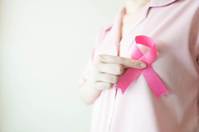 Close-up of a woman in a pink shirt holding a satin pink ribbon, symbolizing breast cancer awareness and support for those considering breast reconstruction after treatment. Close-up of a woman in a pink shirt holding a satin pink ribbon, symbolizing breast cancer awareness and support for those considering breast reconstruction after treatment.